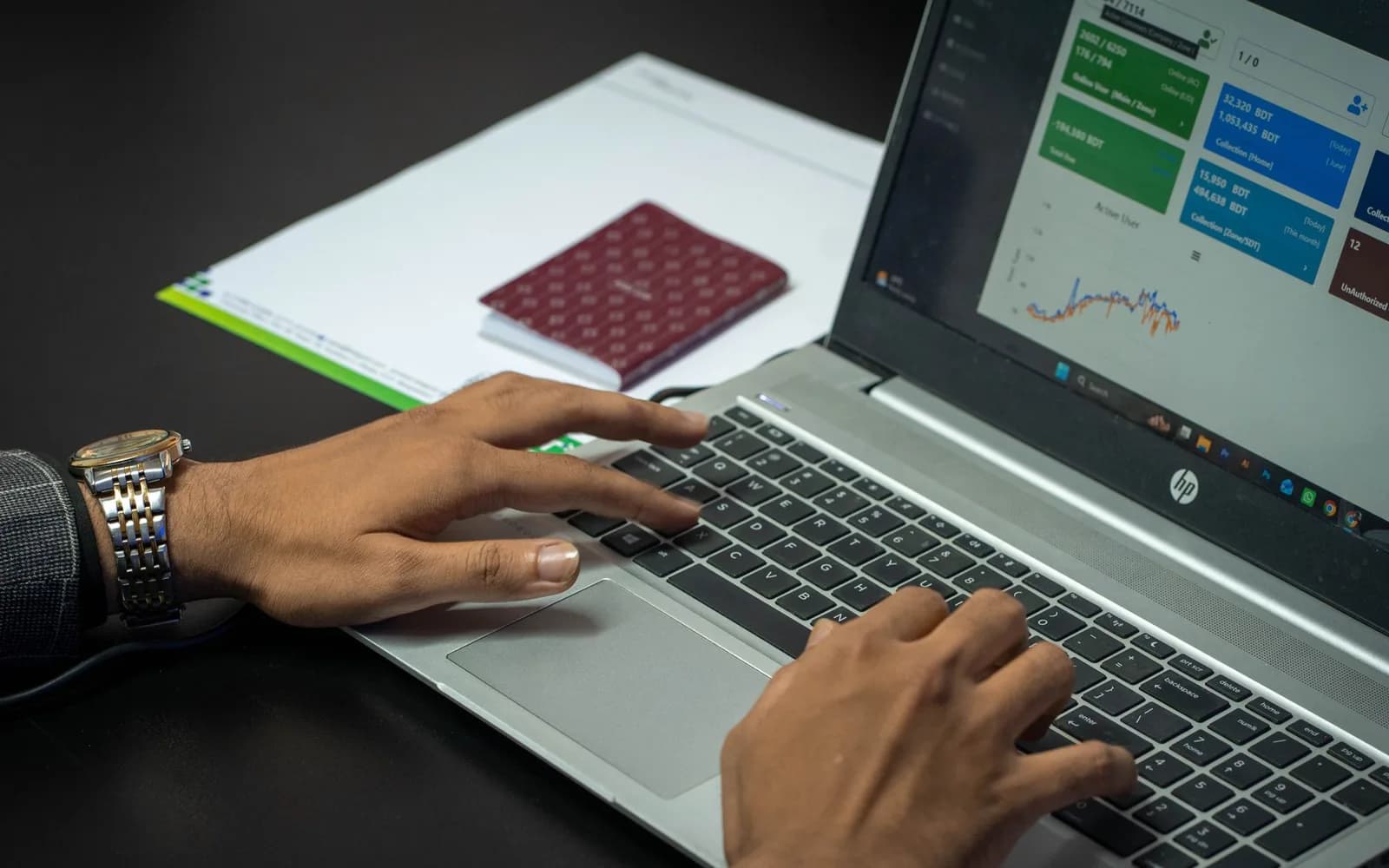 Hands on a laptop keyboard while the screen shows a dashboard with statistics and charts