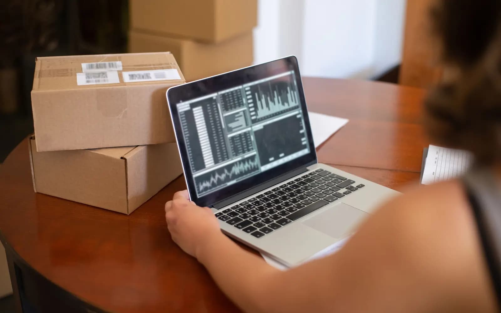 A small business owner reads charts on a laptop next to packed parcels